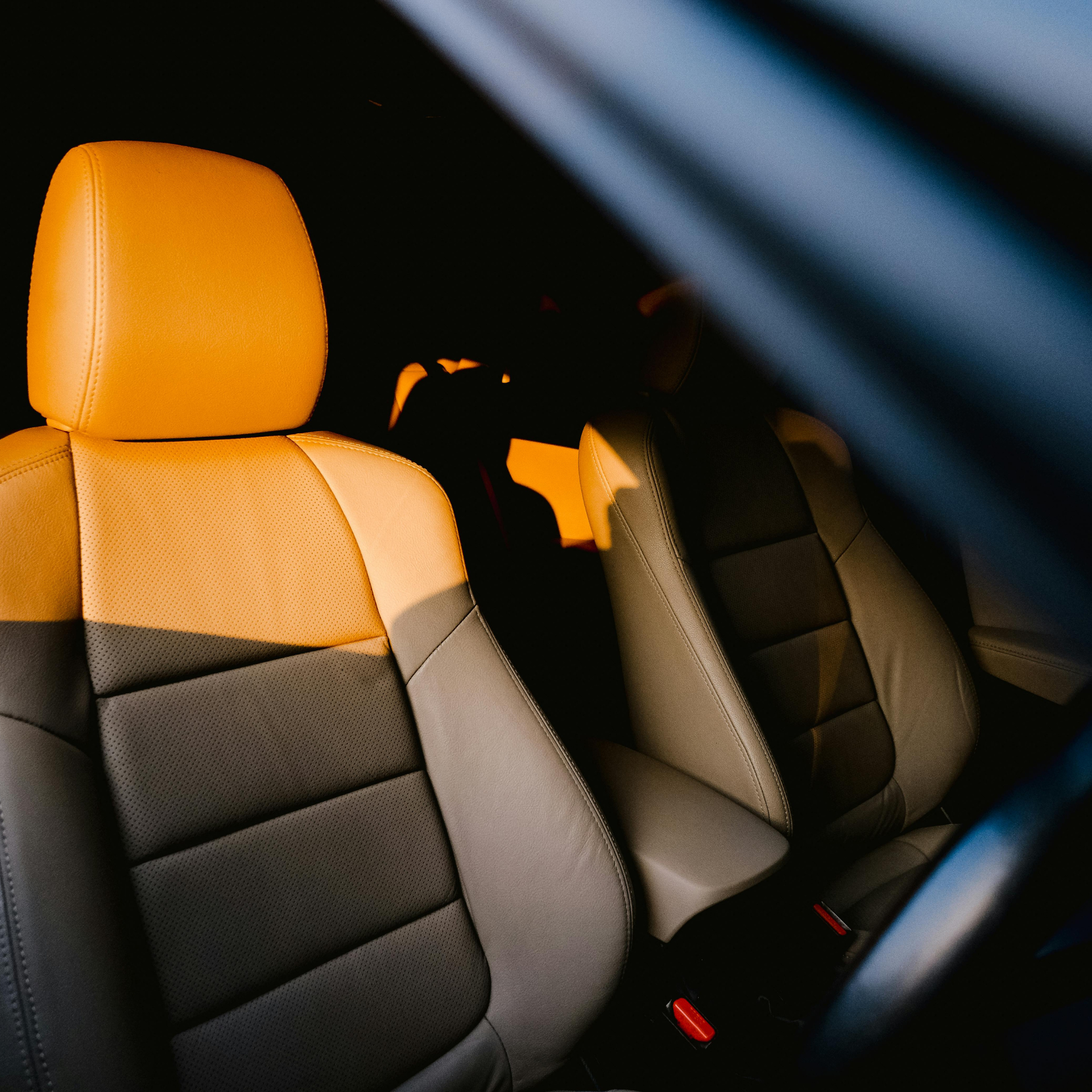 Car interior with gray and tan leather seats, sunlit, shadow in the back.