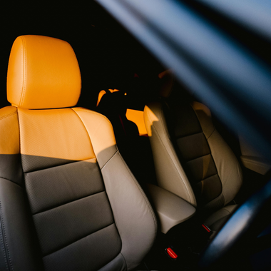 Car interior with gray and tan leather seats, sunlit, shadow in the back.