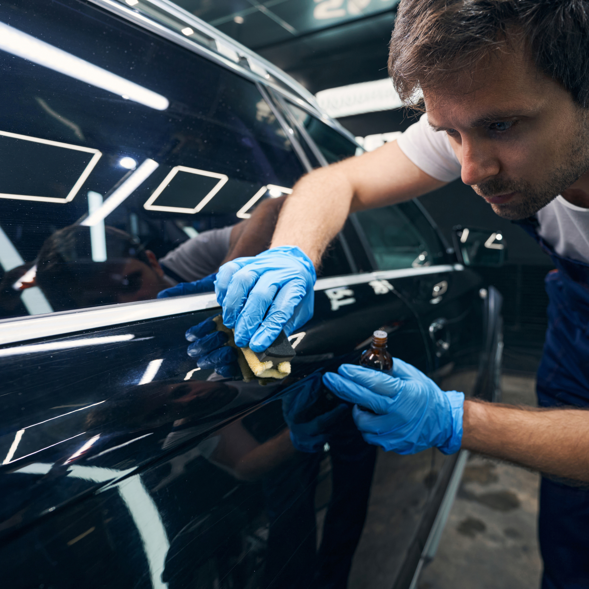 Man applying ceramic coating to a car's door with a sponge, wearing blue gloves.