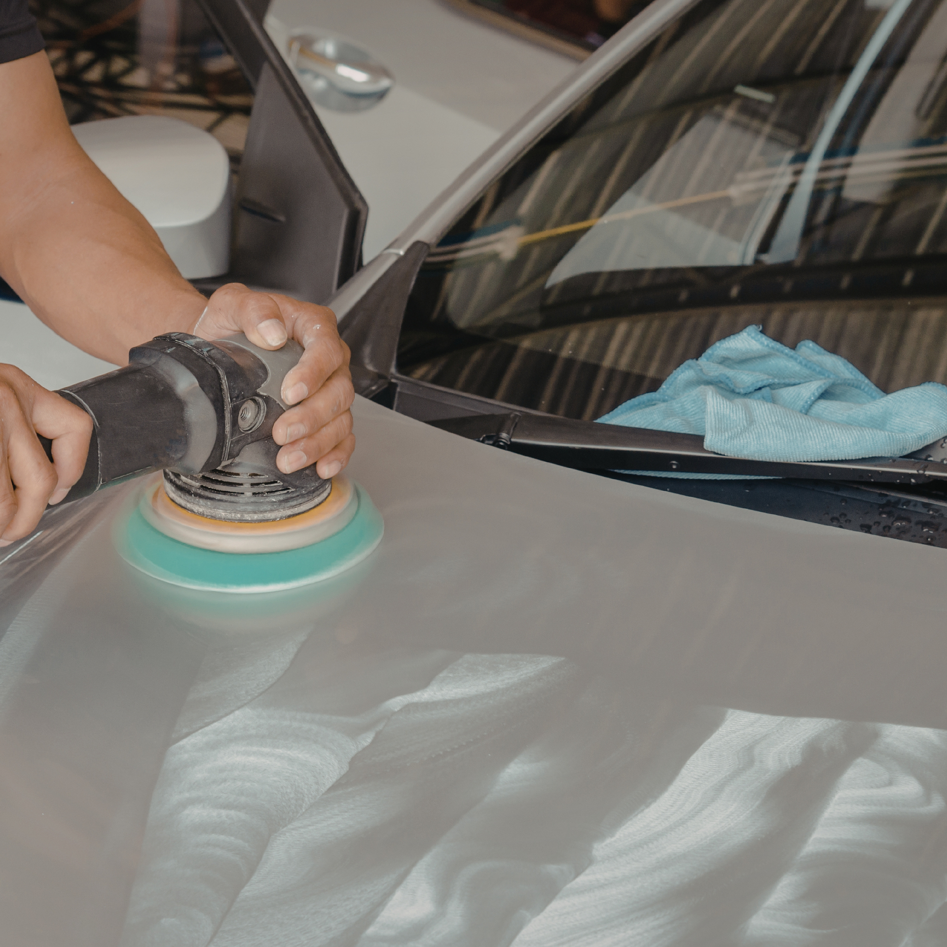Person using a polishing machine on a silver car hood.