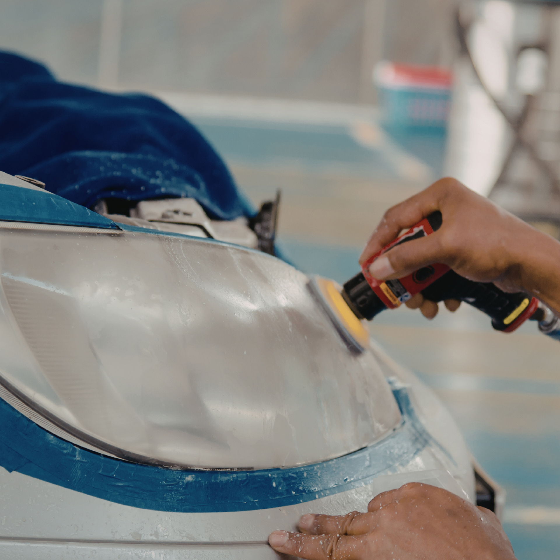 Person polishes a car headlight with a power tool, blue tape visible.