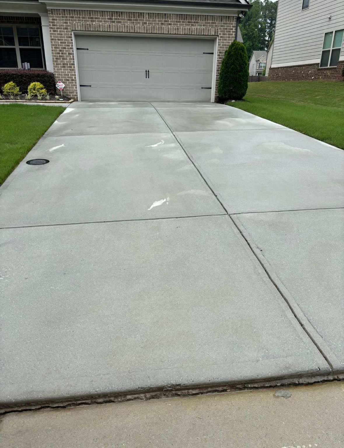 Concrete driveway leading to a closed garage door. Green lawn borders the drive.