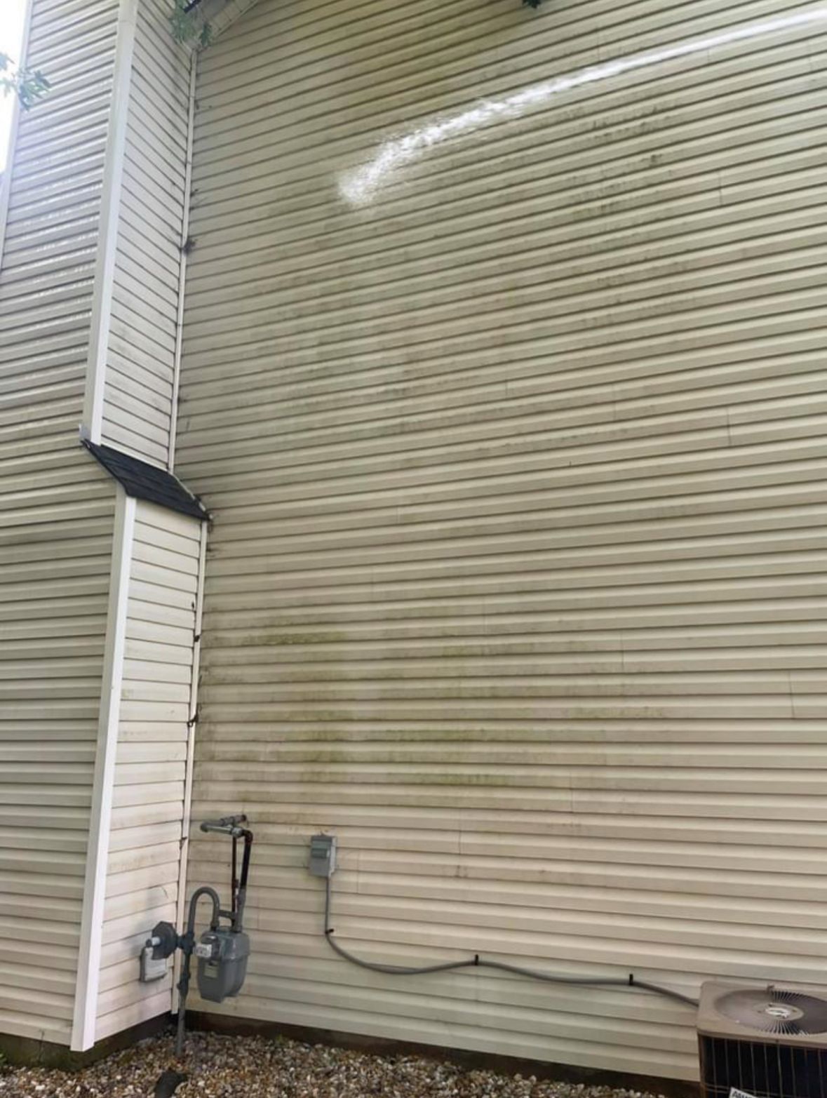 Beige vinyl siding of a house with visible green algae and areas recently cleaned.