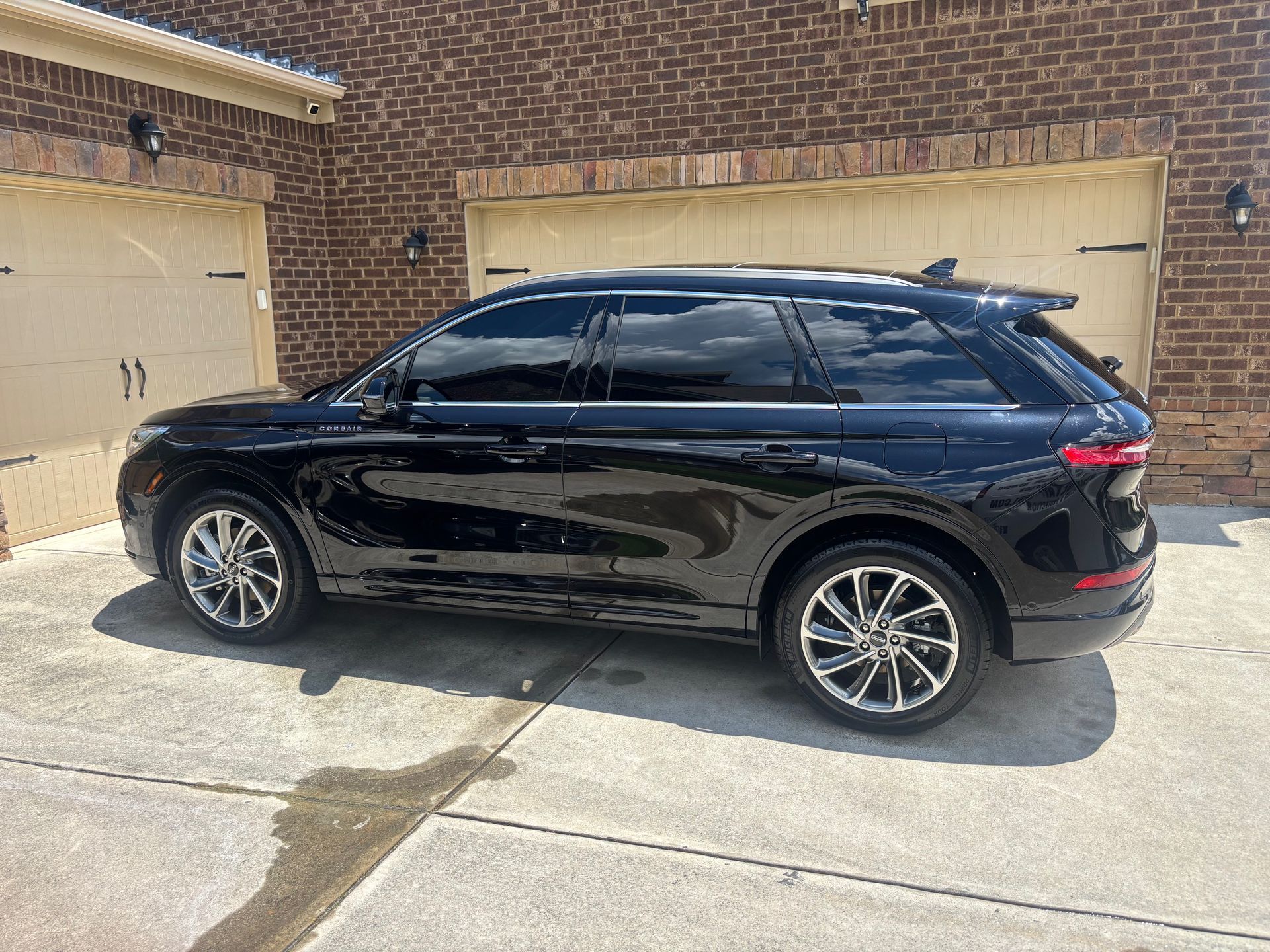Black SUV parked on a concrete driveway in front of a brick building with garage doors.