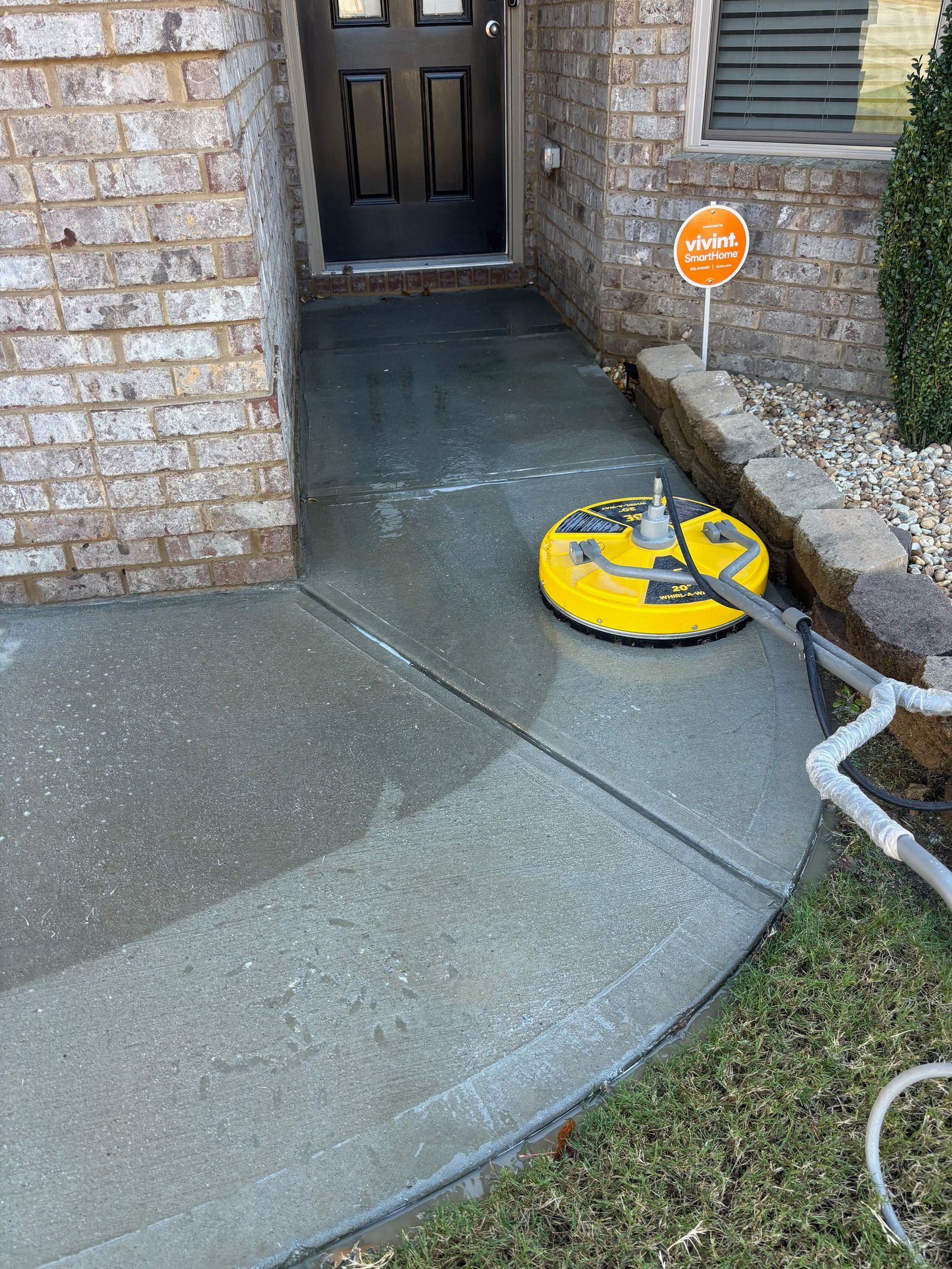 Person power washing a brick driveway near a teal car, water spraying on the pavement.
