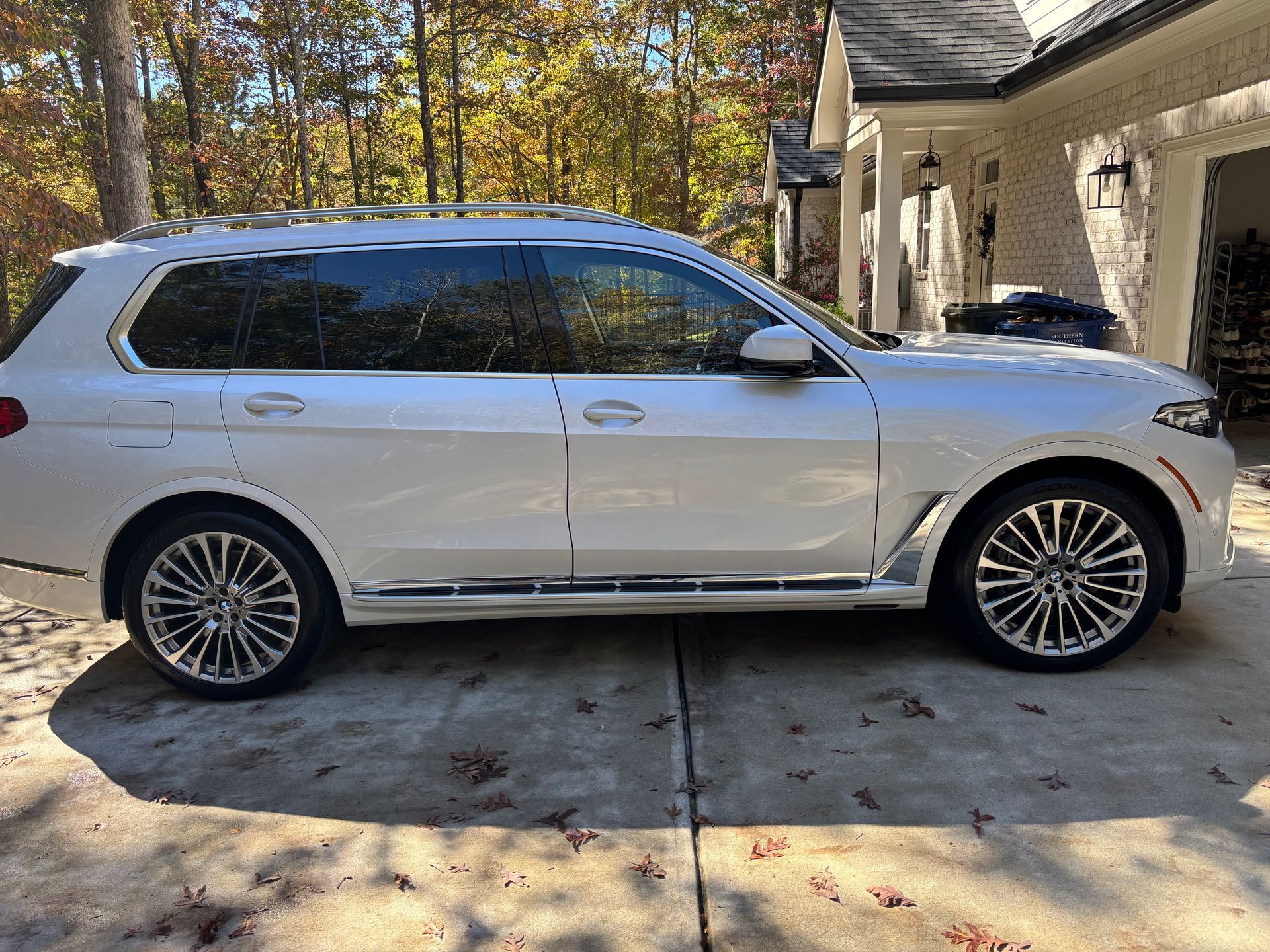 White BMW SUV parked on a concrete driveway in front of a house.