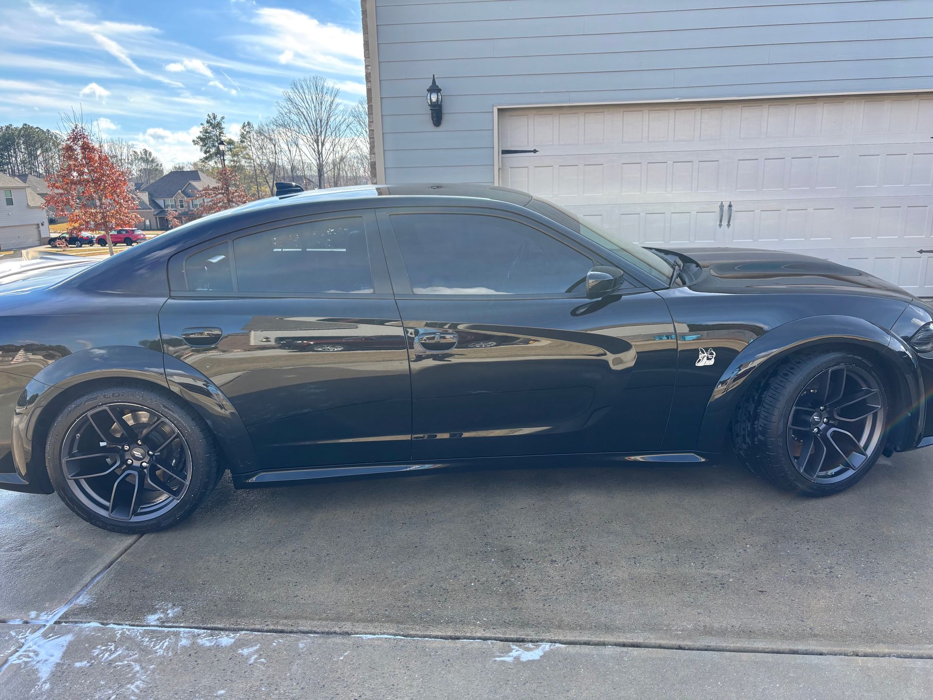 Black sports car parked in front of a garage, with tinted windows and black wheels, set on a sunny day.