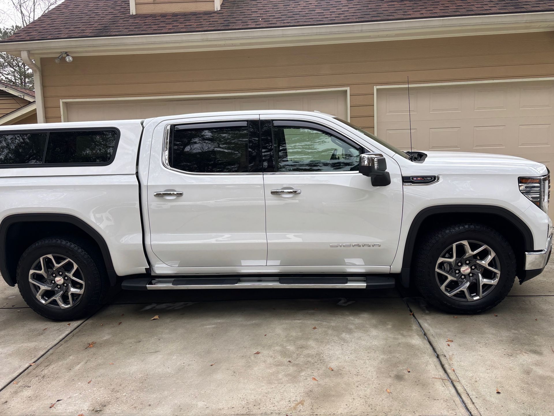 White pickup truck with a cap parked in front of a tan garage.