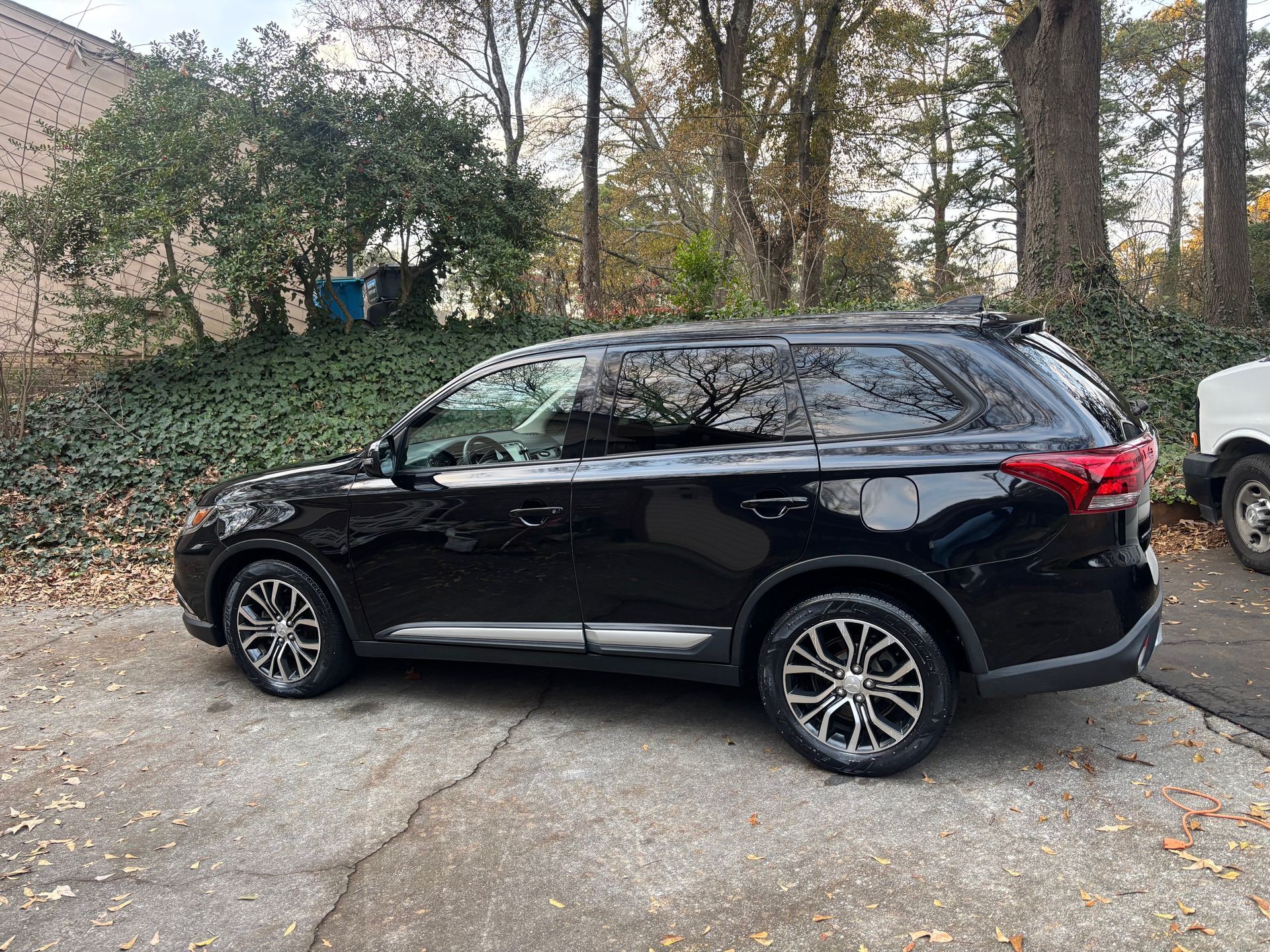 Black SUV parked on a concrete driveway, surrounded by greenery and trees.