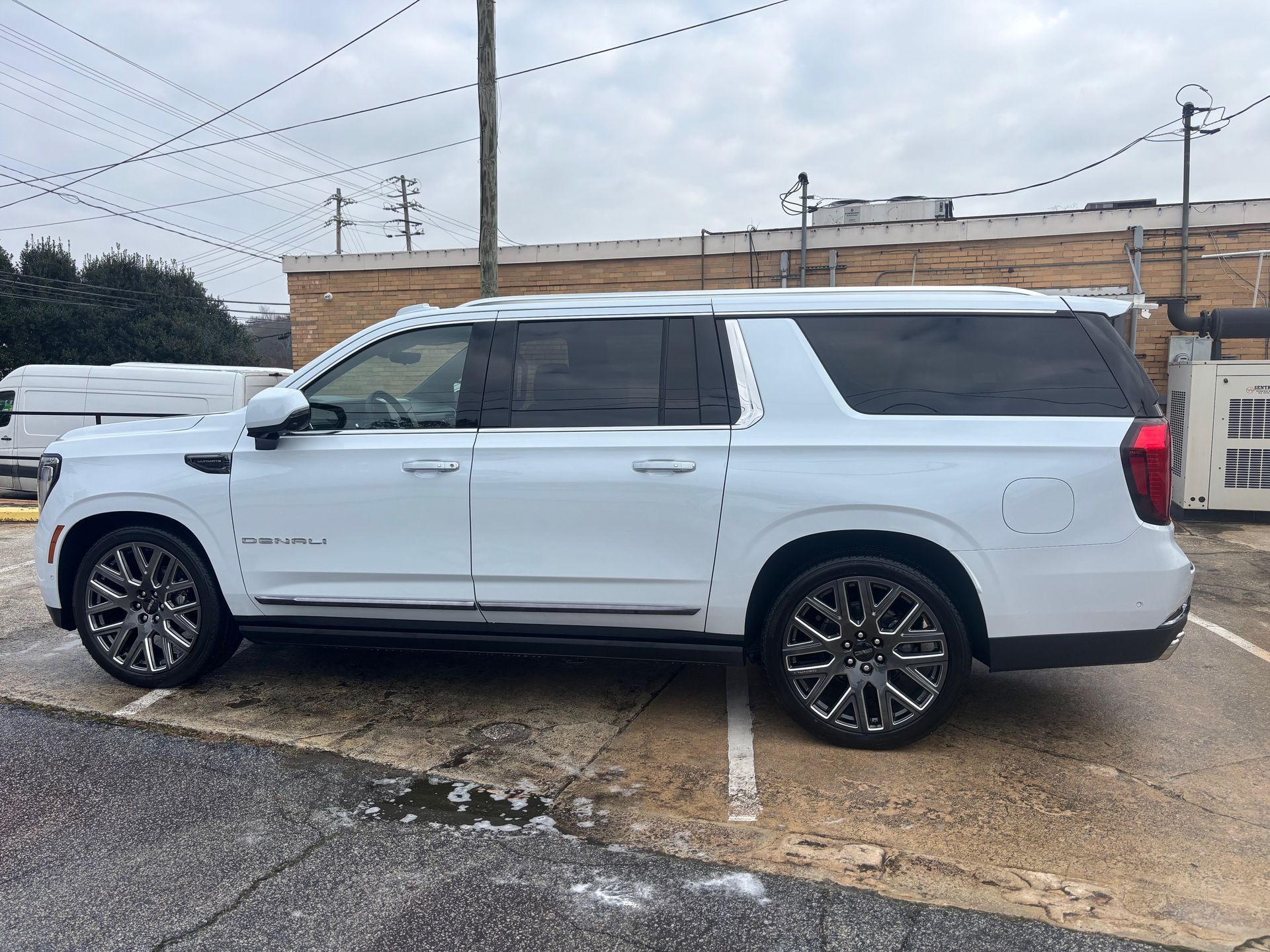 White GMC Yukon SUV parked on a wet surface, overcast sky in background.