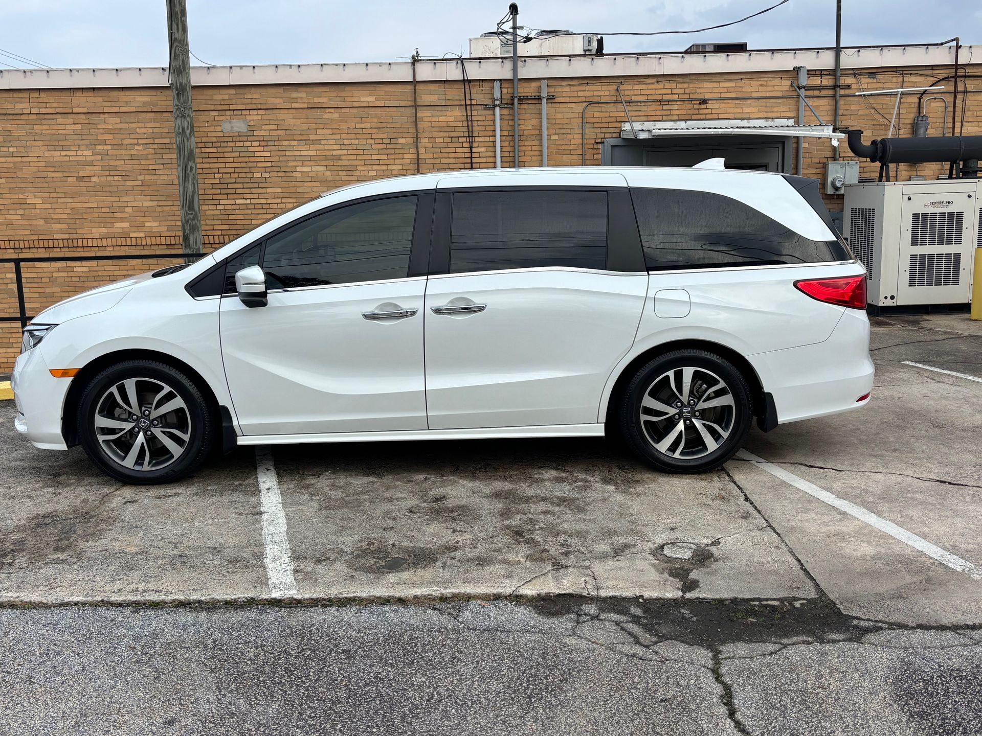 White minivan parked in a lot, against a brick wall. Dark tinted windows and black rims are visible.