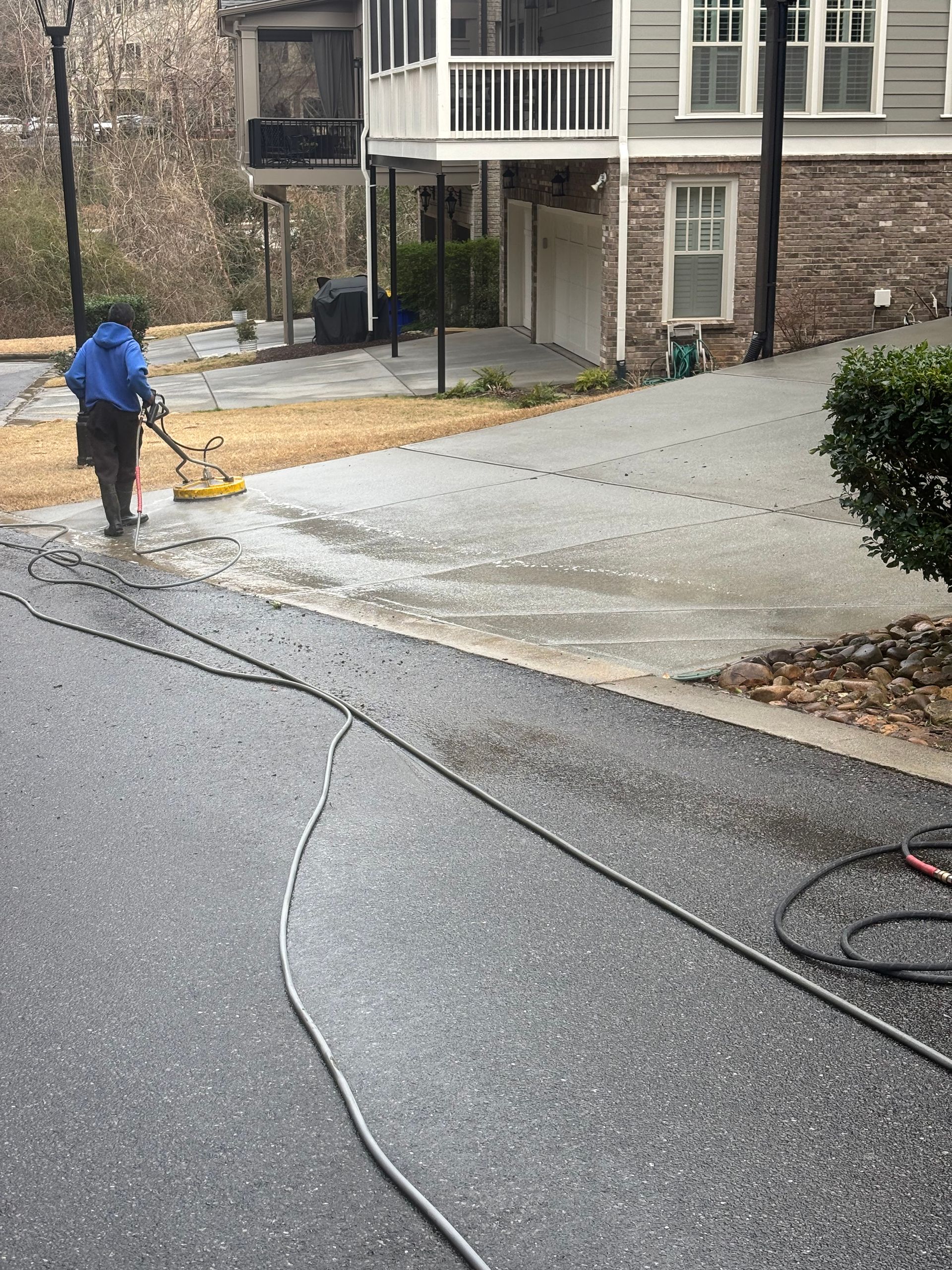 Person power washing a brick driveway near a teal car, water spraying on the pavement.