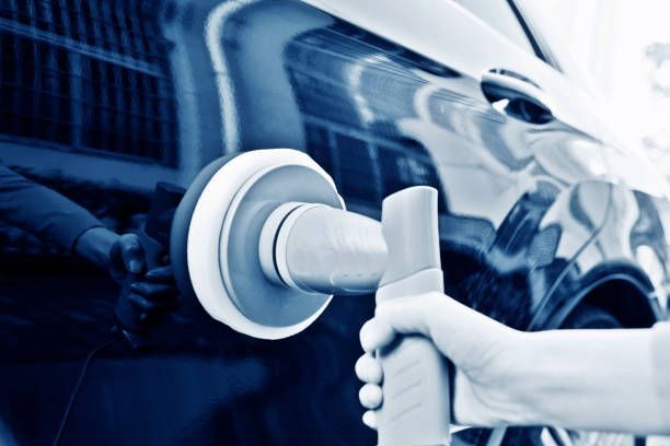 Person hand-applying a blue applicator pad to a black car's body.