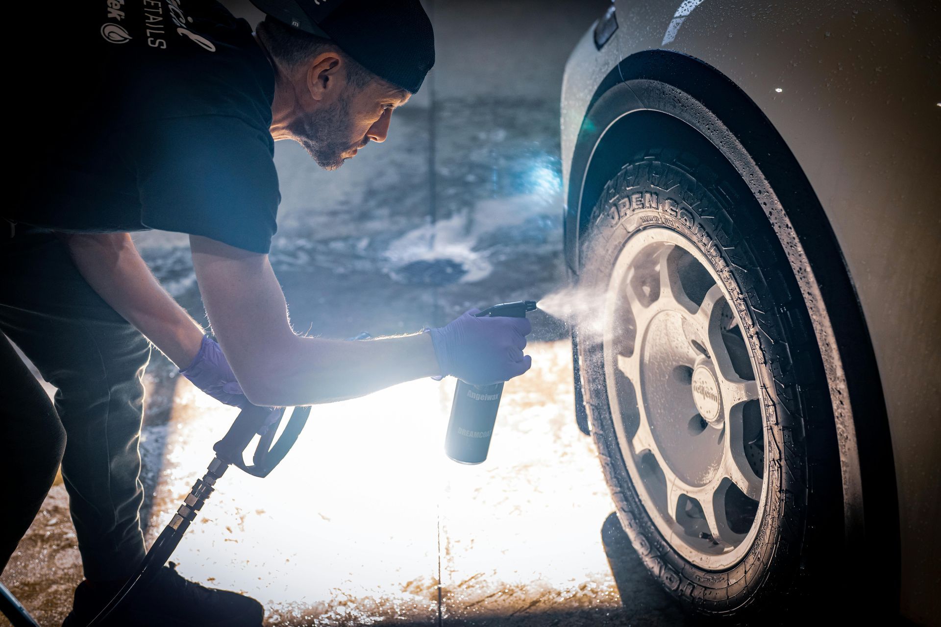 Man spraying a car tire with a pressure washer; outdoors, washing a white car's wheel.