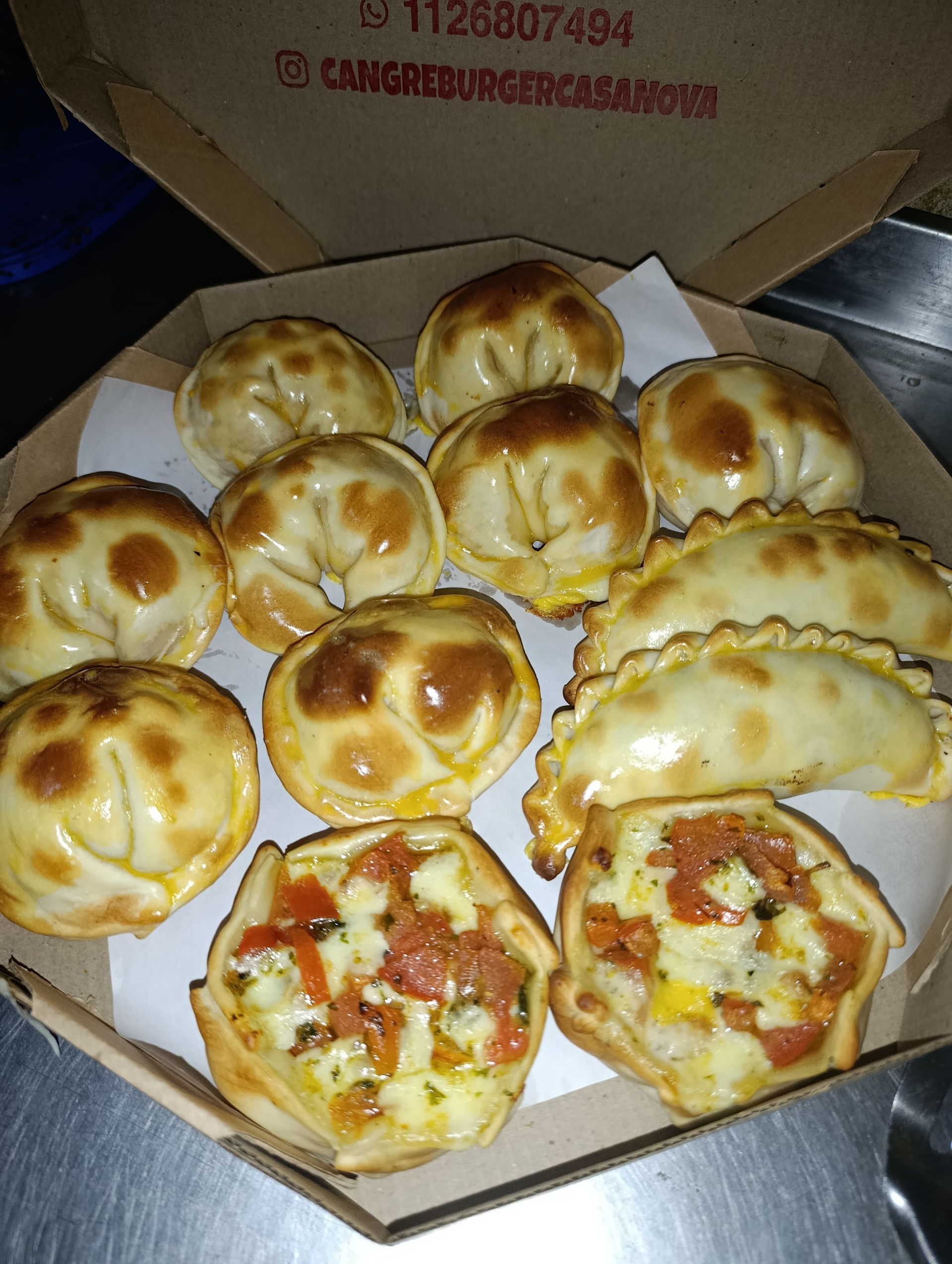Surtido de empanadas horneadas y pizzas pequeñas en caja de cartón; masa de color marrón dorado.