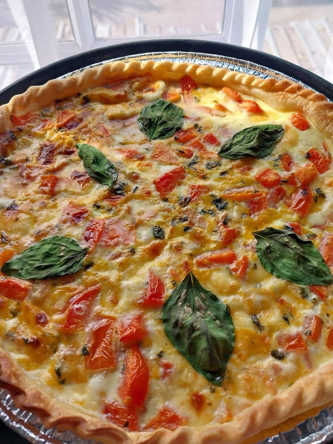 Quiche de tomate y albahaca en masa de tarta, adornada con hojas de albahaca fresca.