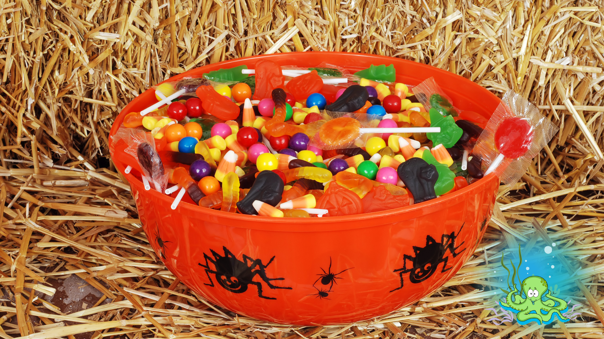 Orange Halloween candy bowl filled with sweets against a hay background.