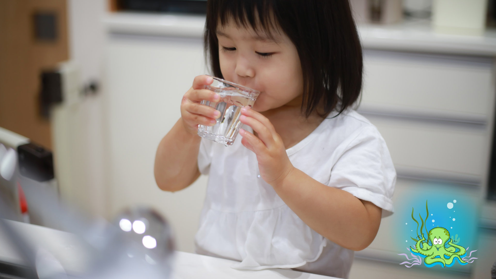 Child drinking water from a glass by a kitchen sink.