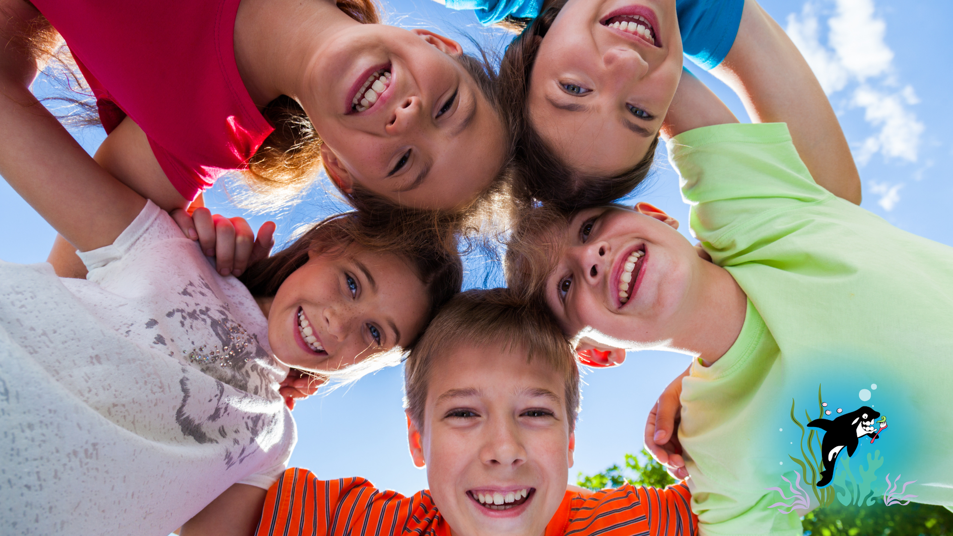Children smiling, looking down toward the camera, in a circle, against a bright blue sky.