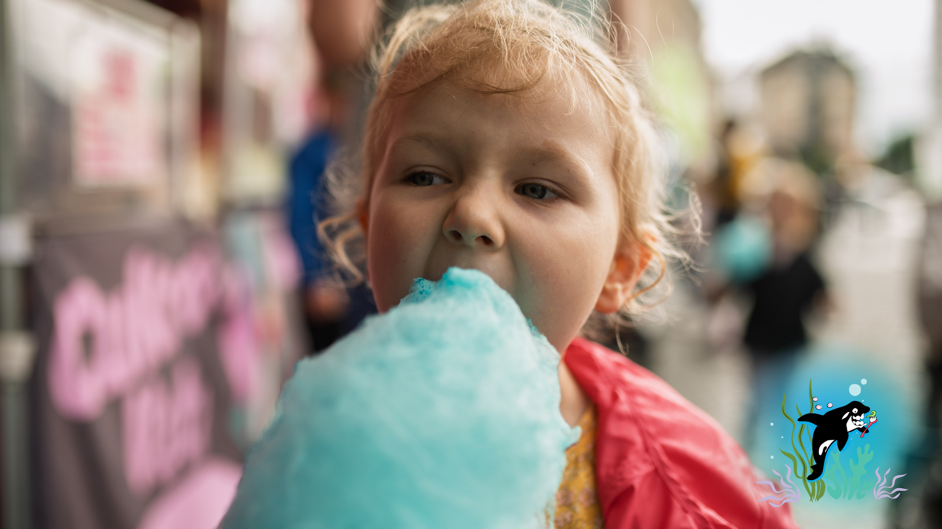 Blond child eating blue cotton candy at an outdoor event, pink jacket, close-up.