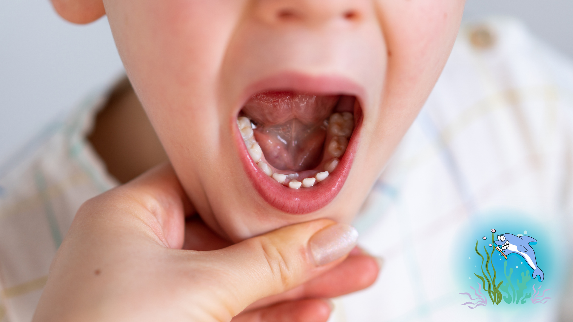 Child's open mouth showing teeth, hand under chin.
