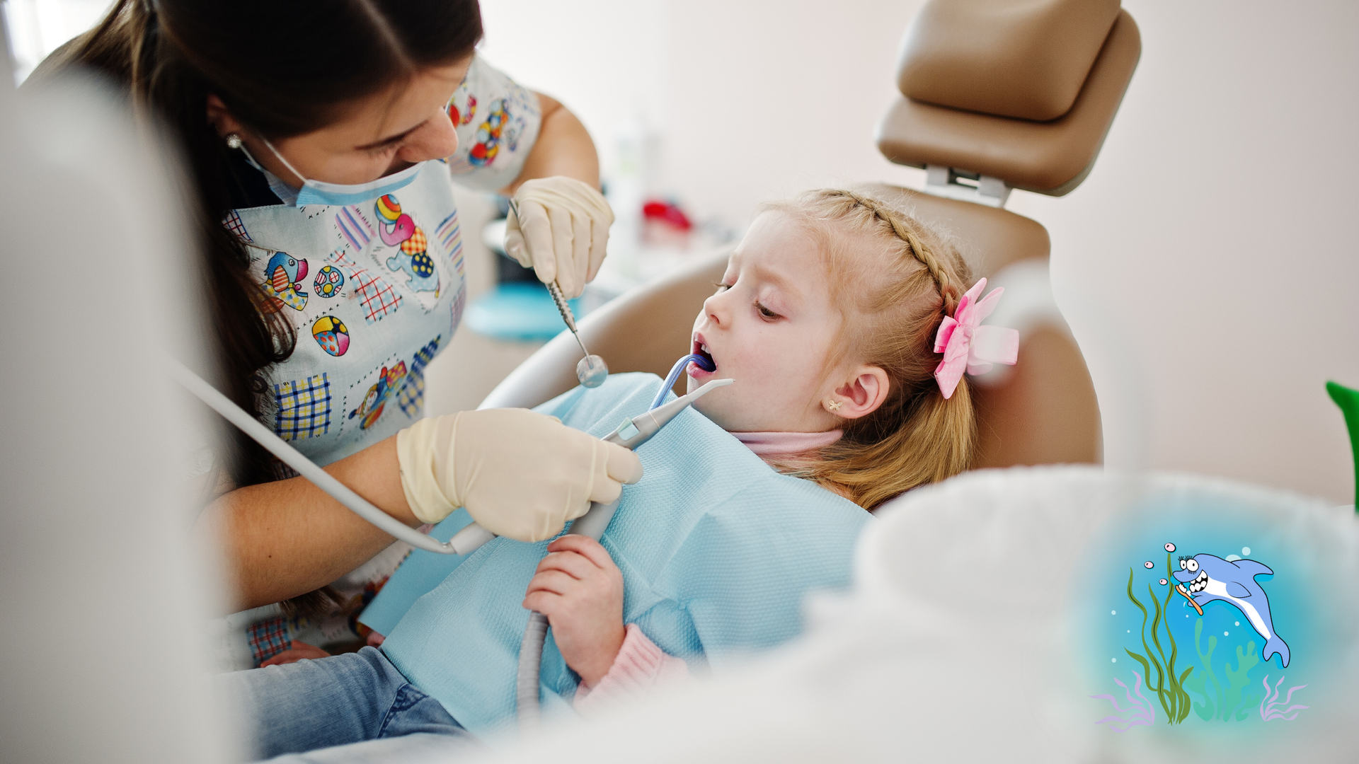 Dentist examining a child's teeth in a dental chair. The child has her mouth open. The dentist wears a mask and gloves.
