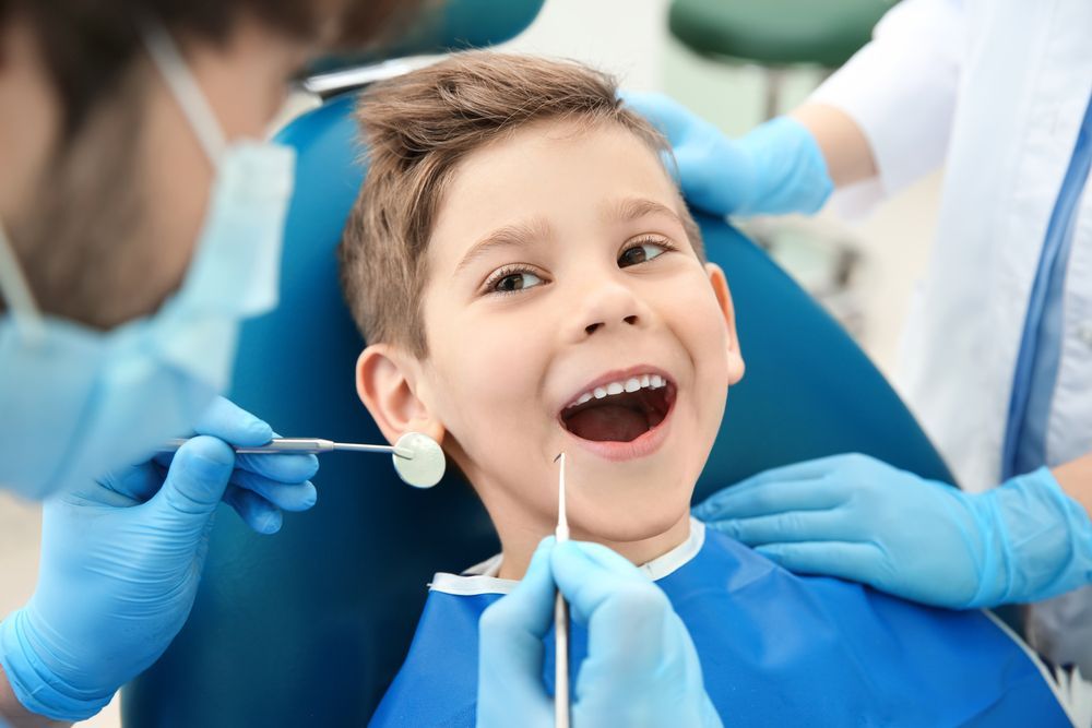 A young boy is sitting in a dental chair while a dentist examines his teeth.