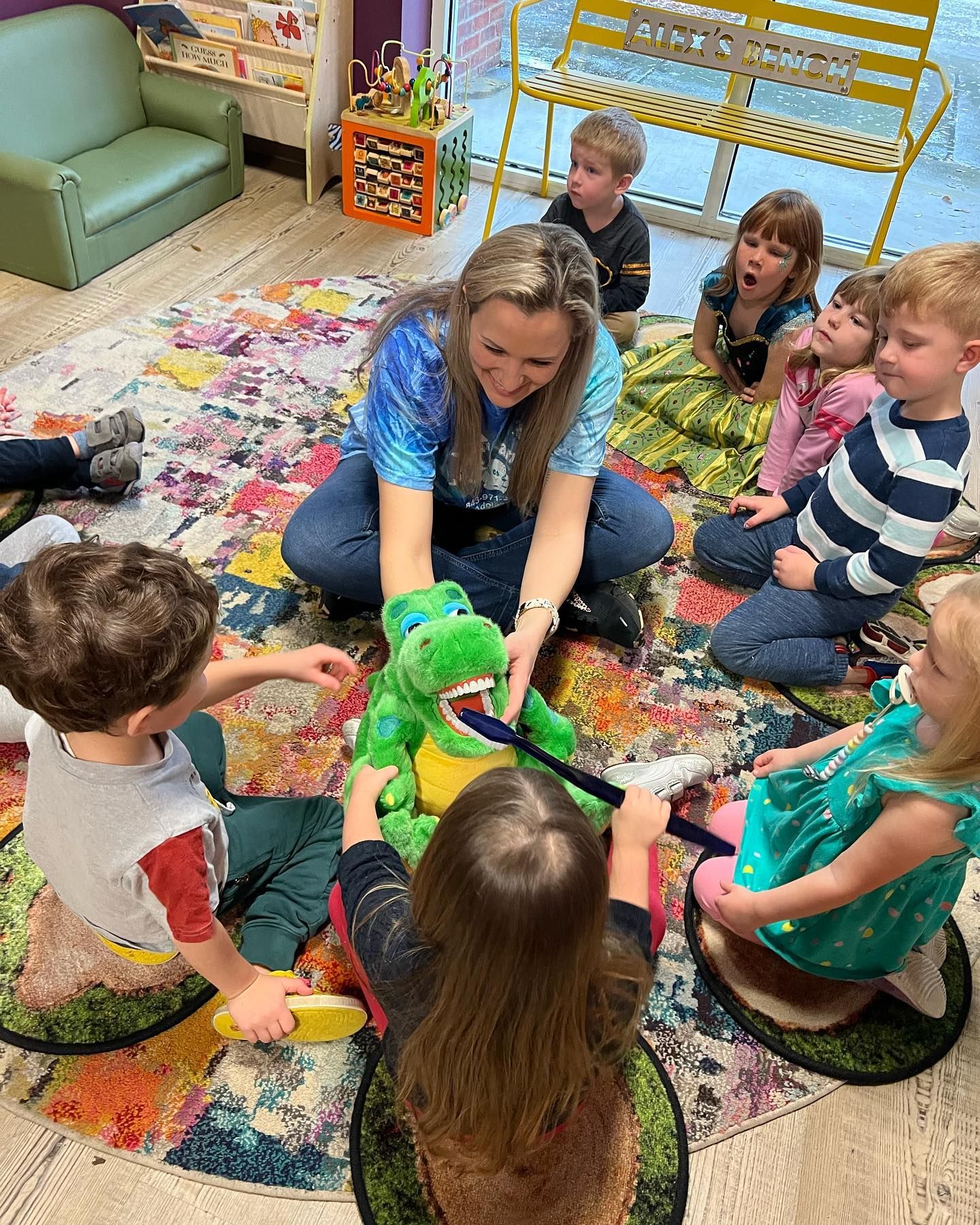 A group of children are sitting on the floor playing with a stuffed dinosaur.