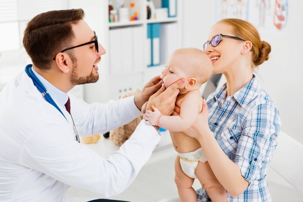 Doctor examining a baby held by a smiling parent in a doctor's office.