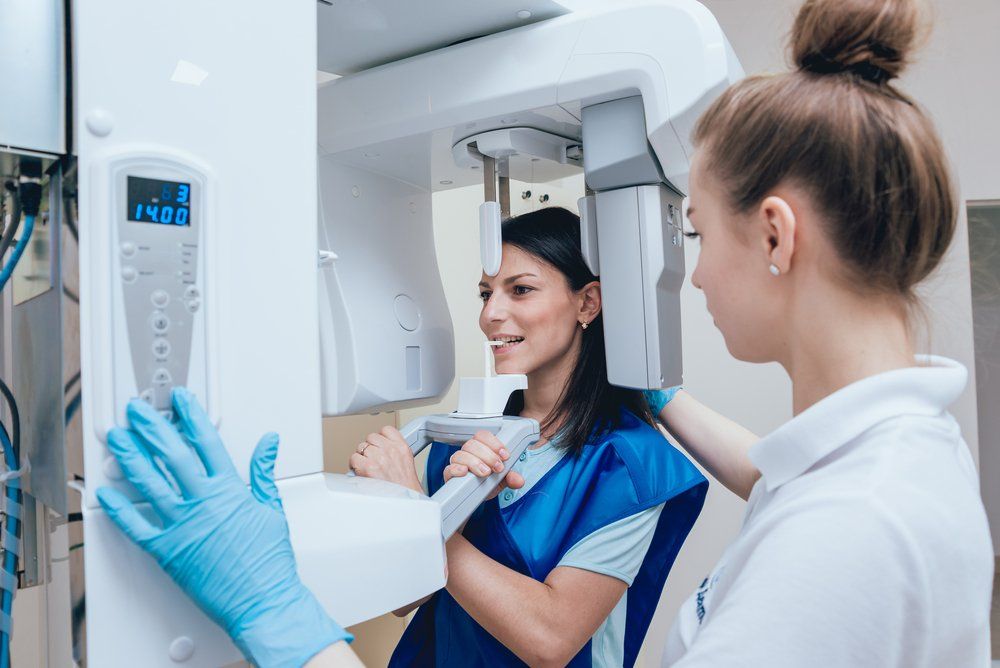 Woman receiving a dental panoramic X-ray from a dental professional. Blue gloves, patient smiles, white machine.