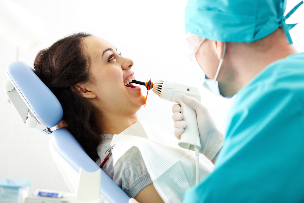 Dentist using a curing light on a patient's open mouth in a dental office.