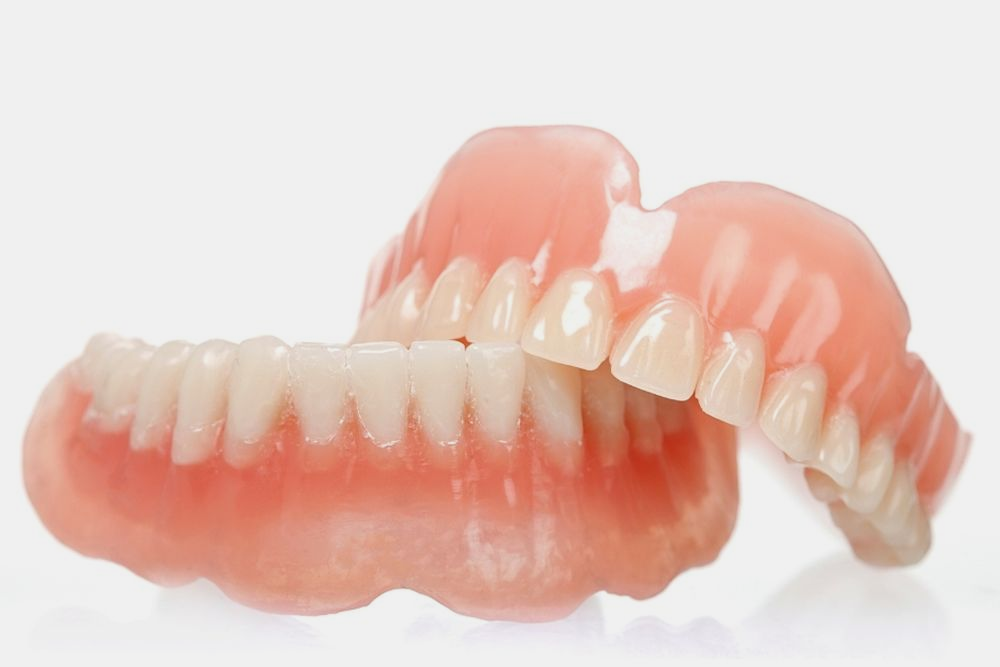 Dentures: upper and lower sets with pink gum-colored bases and rows of white teeth, resting against each other.