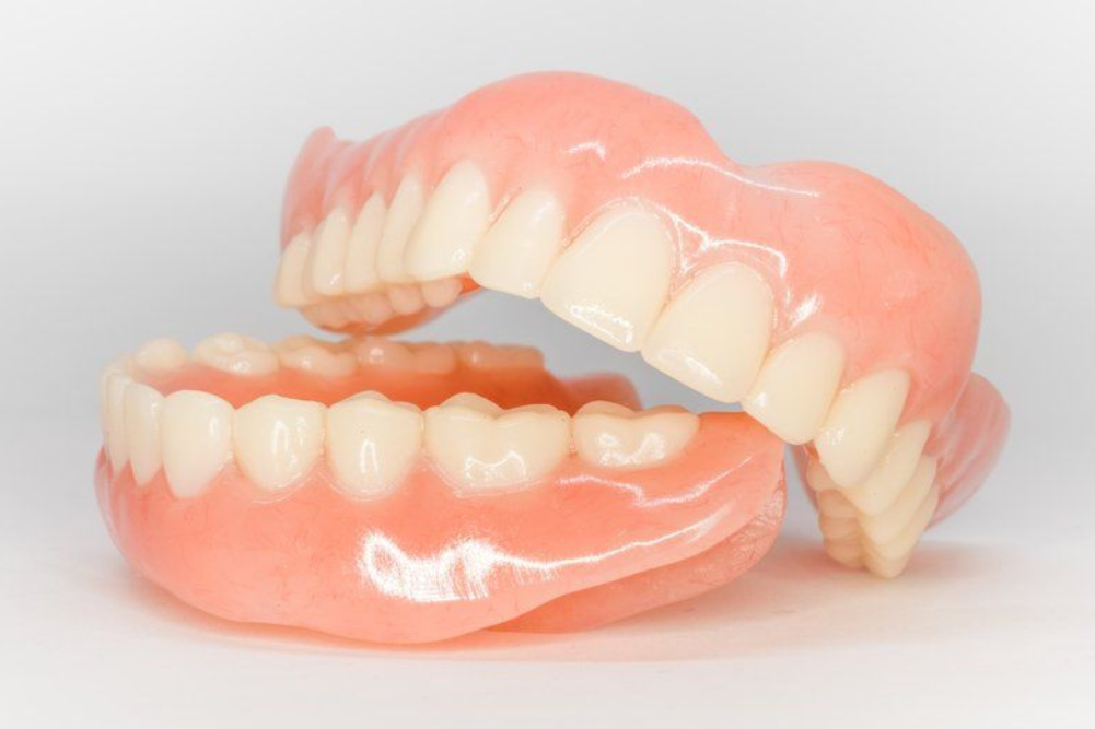 Pair of dentures, pink base, white artificial teeth, against a white background.