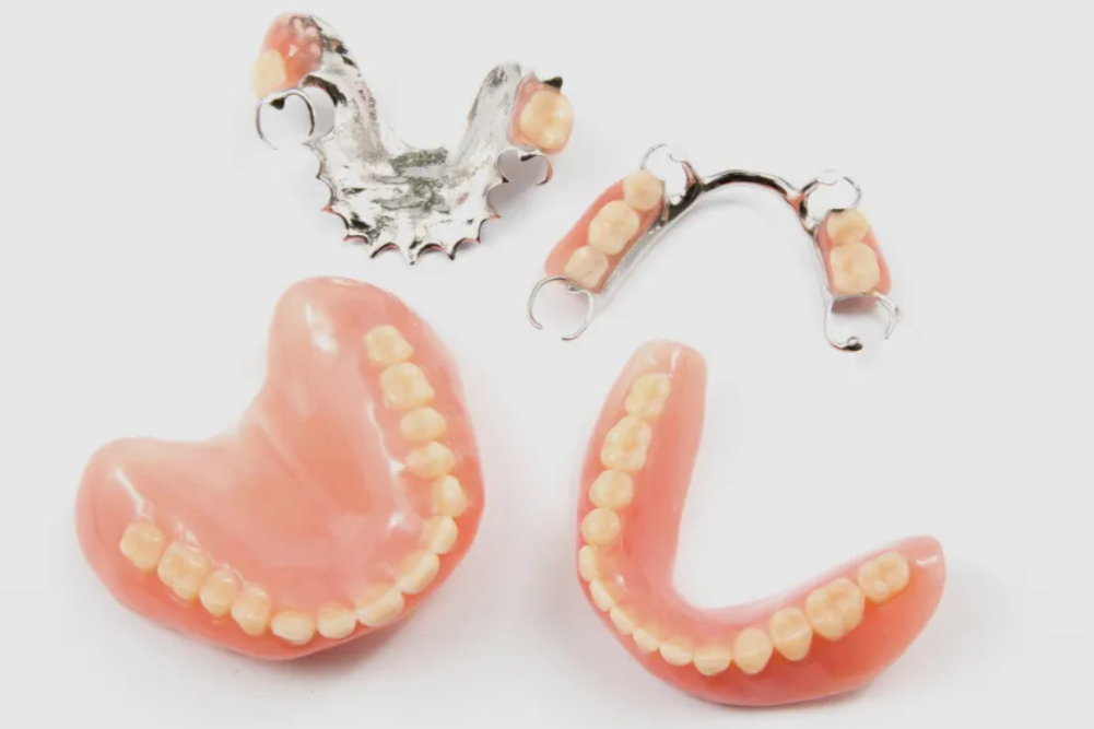 Dentures, partial dentures displayed on a white surface. The dentures are pink with beige teeth.
