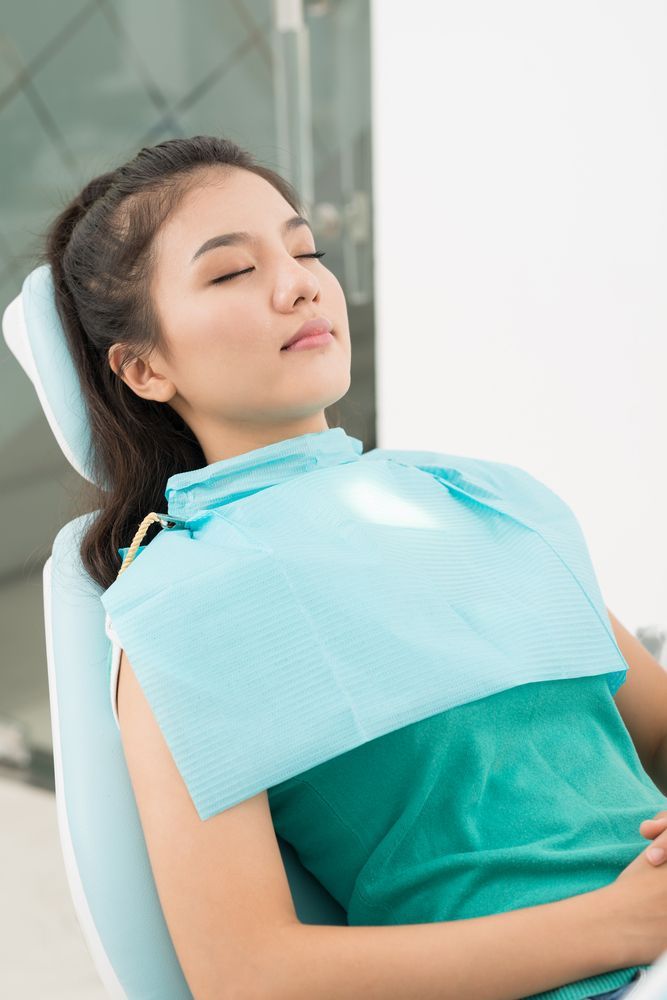 Woman in dentist chair, eyes closed, wearing a dental bib.