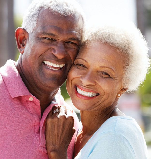 Smiling couple embraces outdoors, one in pink shirt, the other in a blue top.