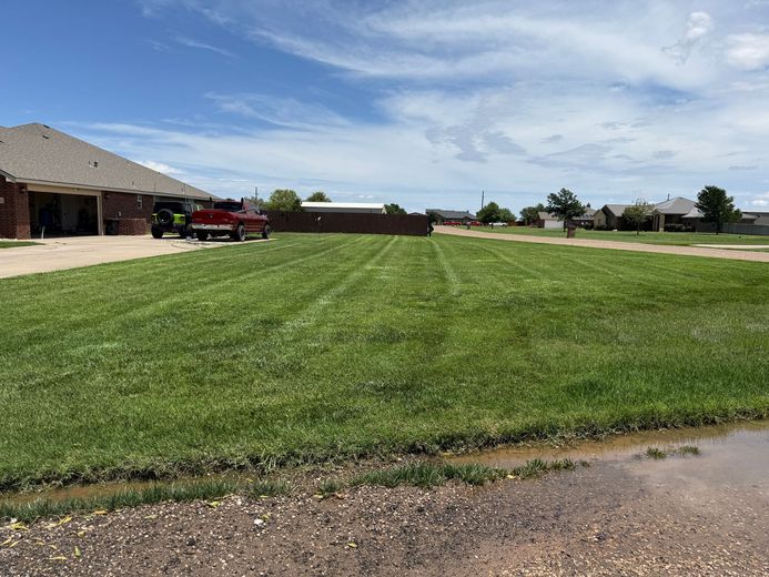 Lawn with fresh mowing stripes. Brick home with truck in driveway on left, other houses on right. Cloudy sky.
