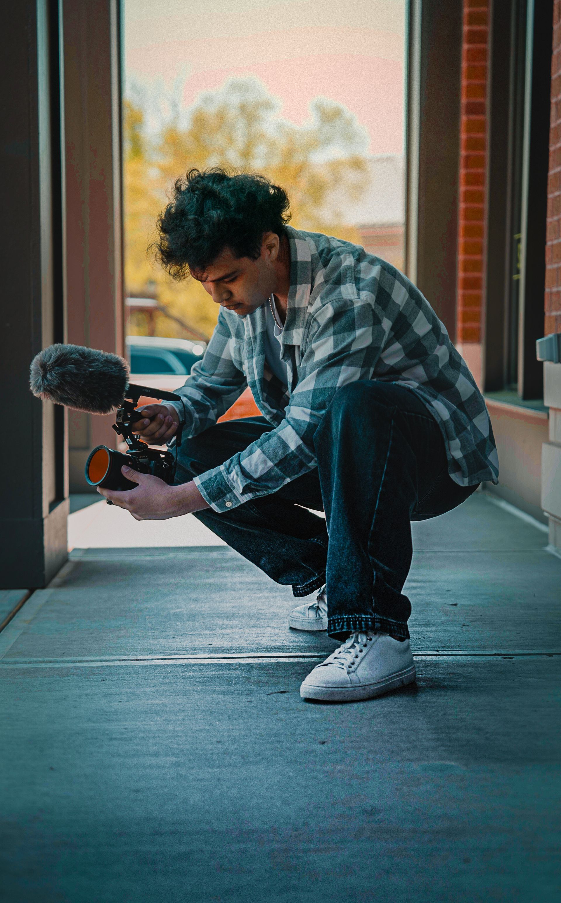 A man is squatting down while holding a camera and a microphone.