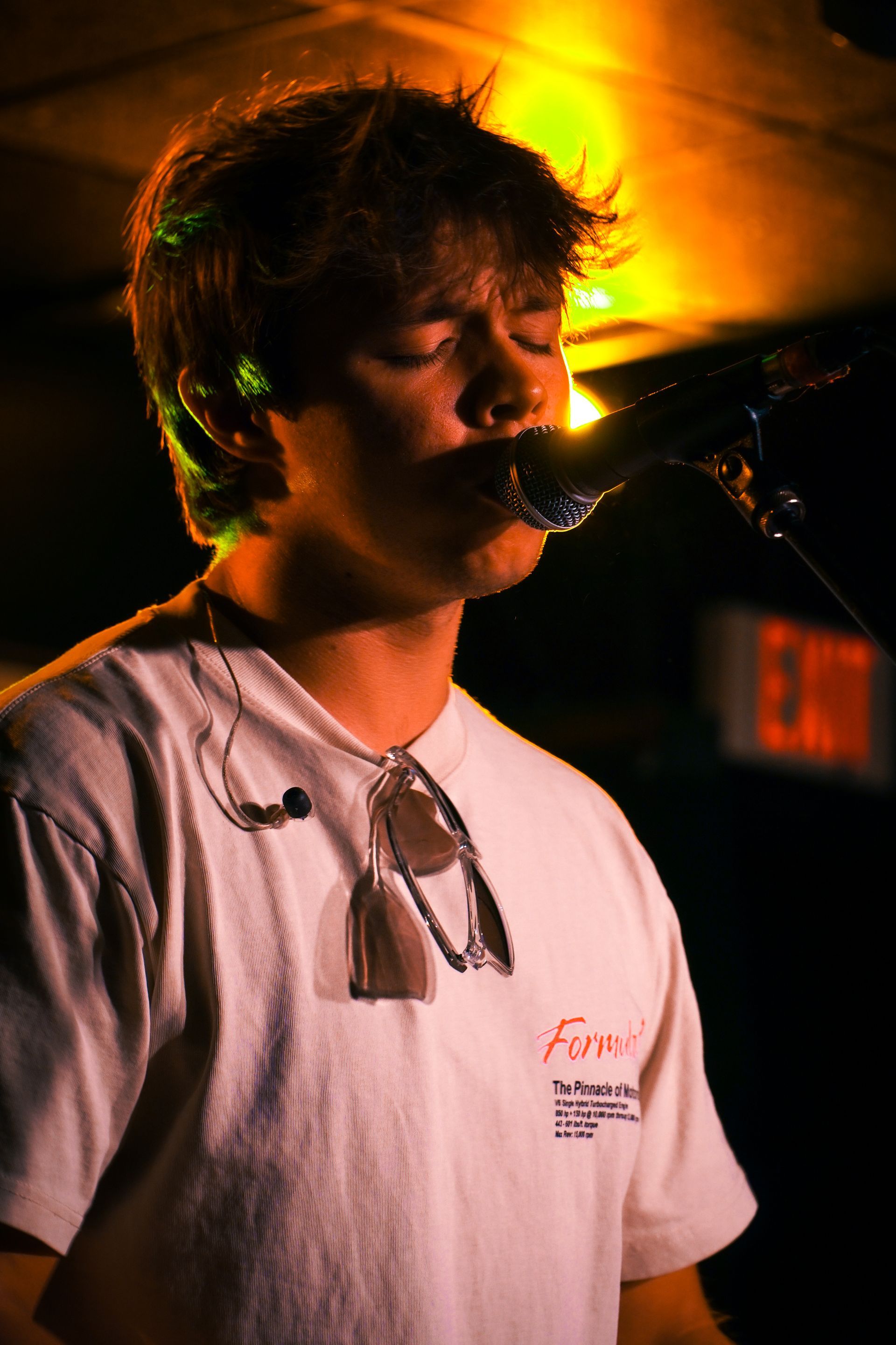 A young man is singing into a microphone in a dark room.