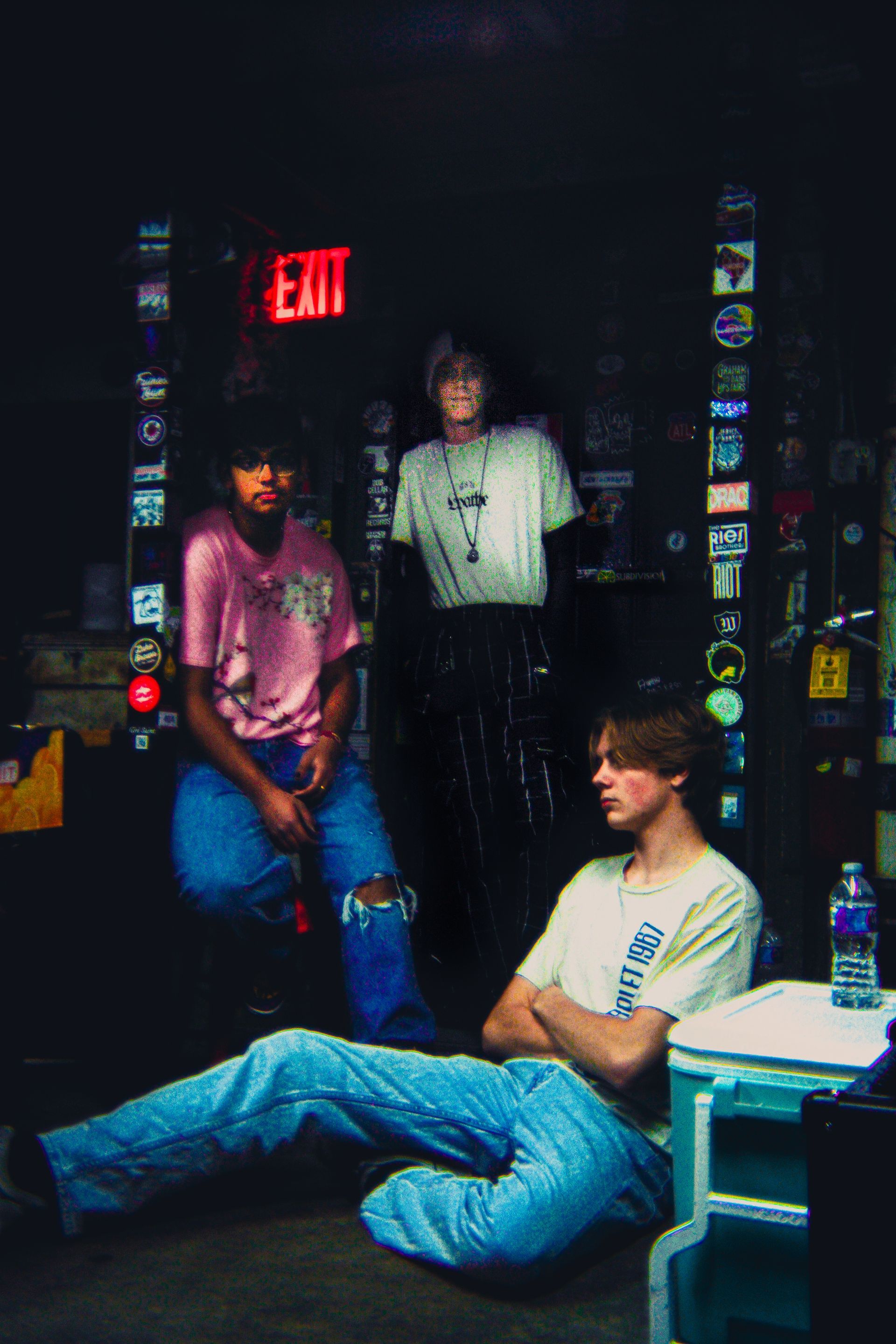 Three people are sitting on the floor in front of an exit sign.