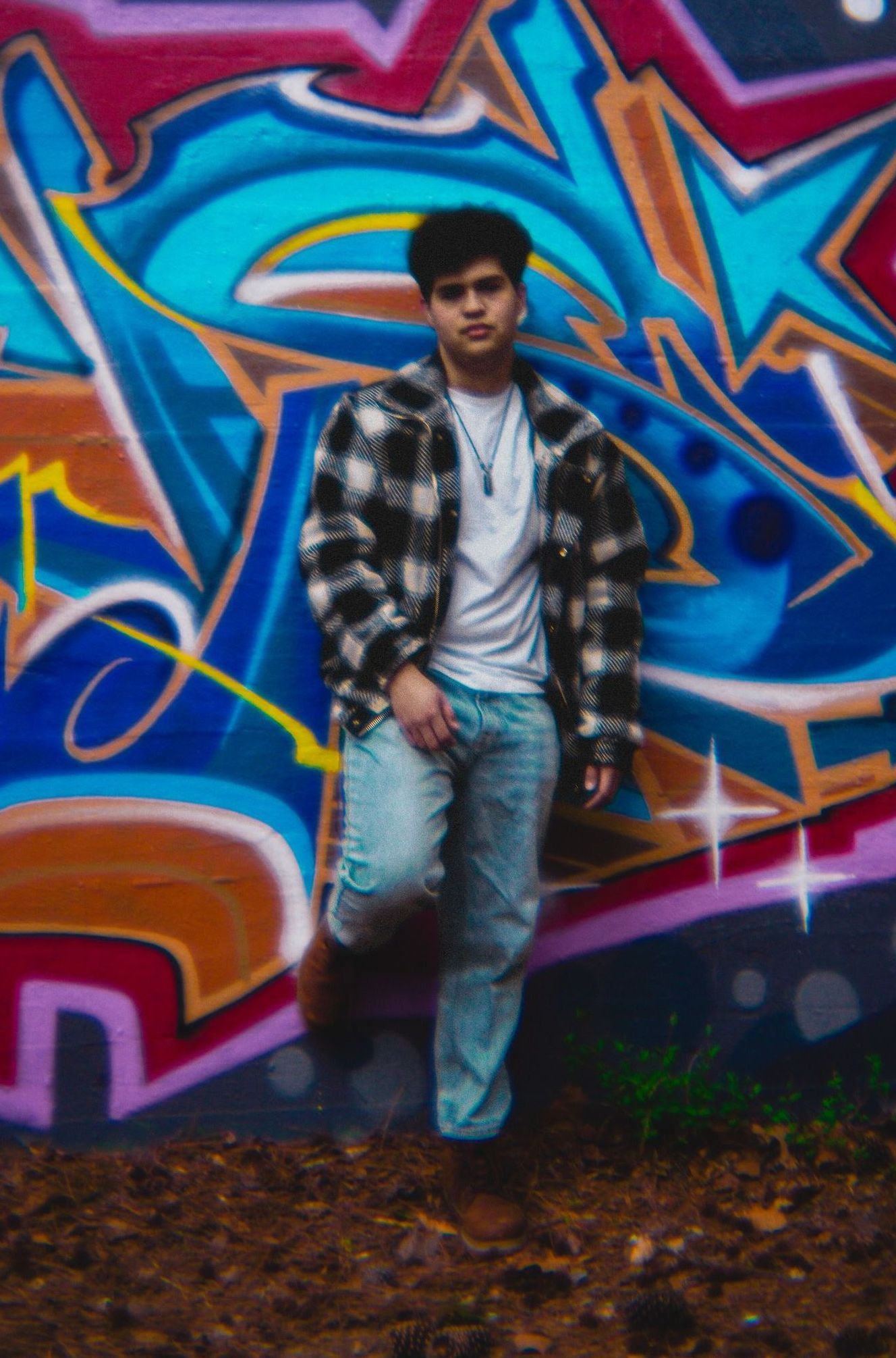 A young man is standing in front of a graffiti wall.