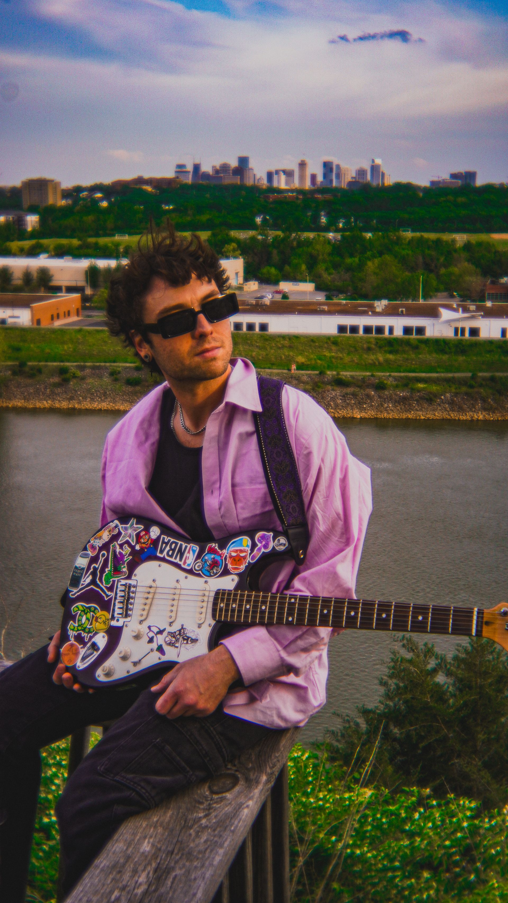 A man is sitting on a railing holding a guitar.