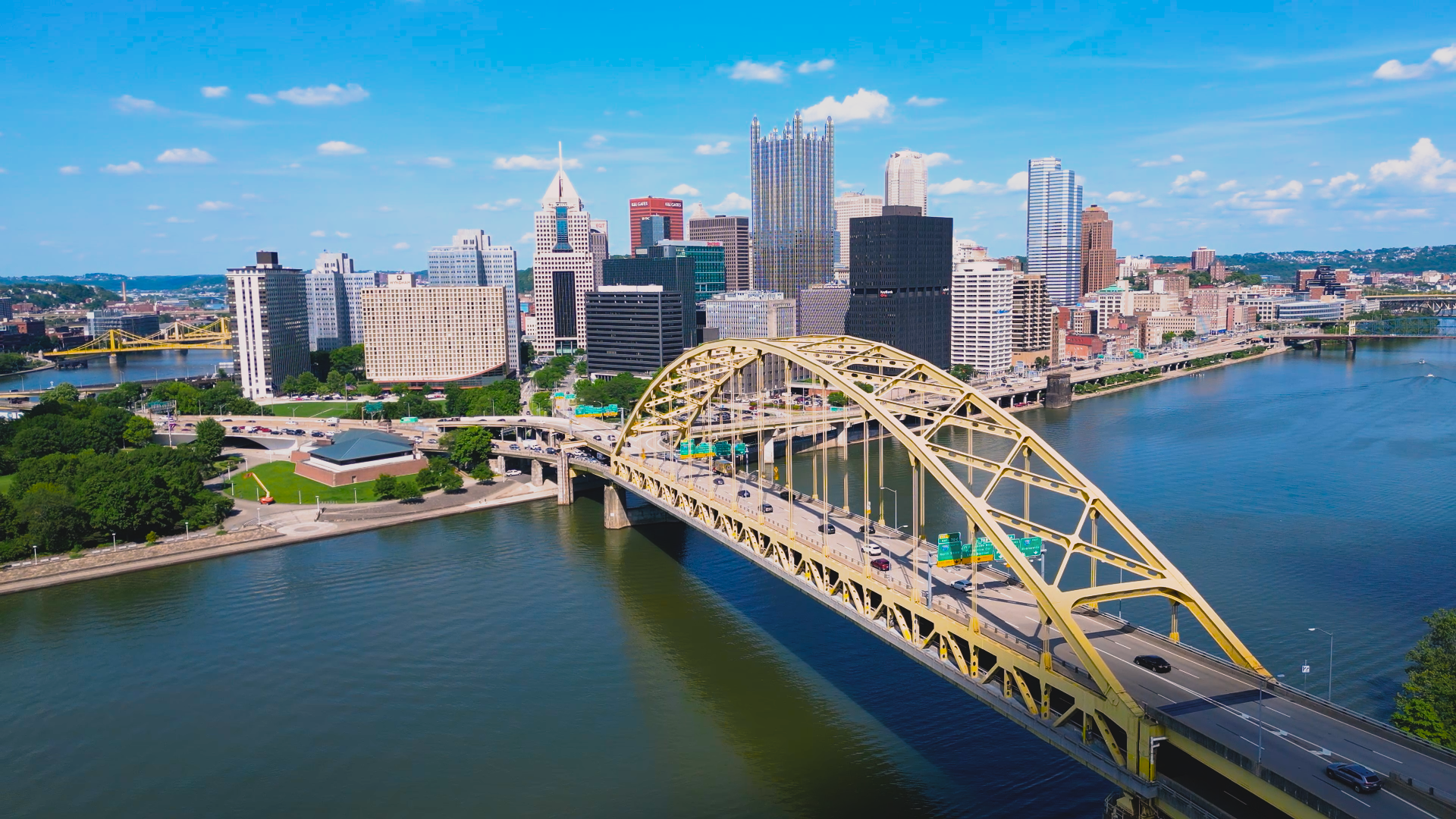An aerial view of a bridge over a river with a city skyline in the background.