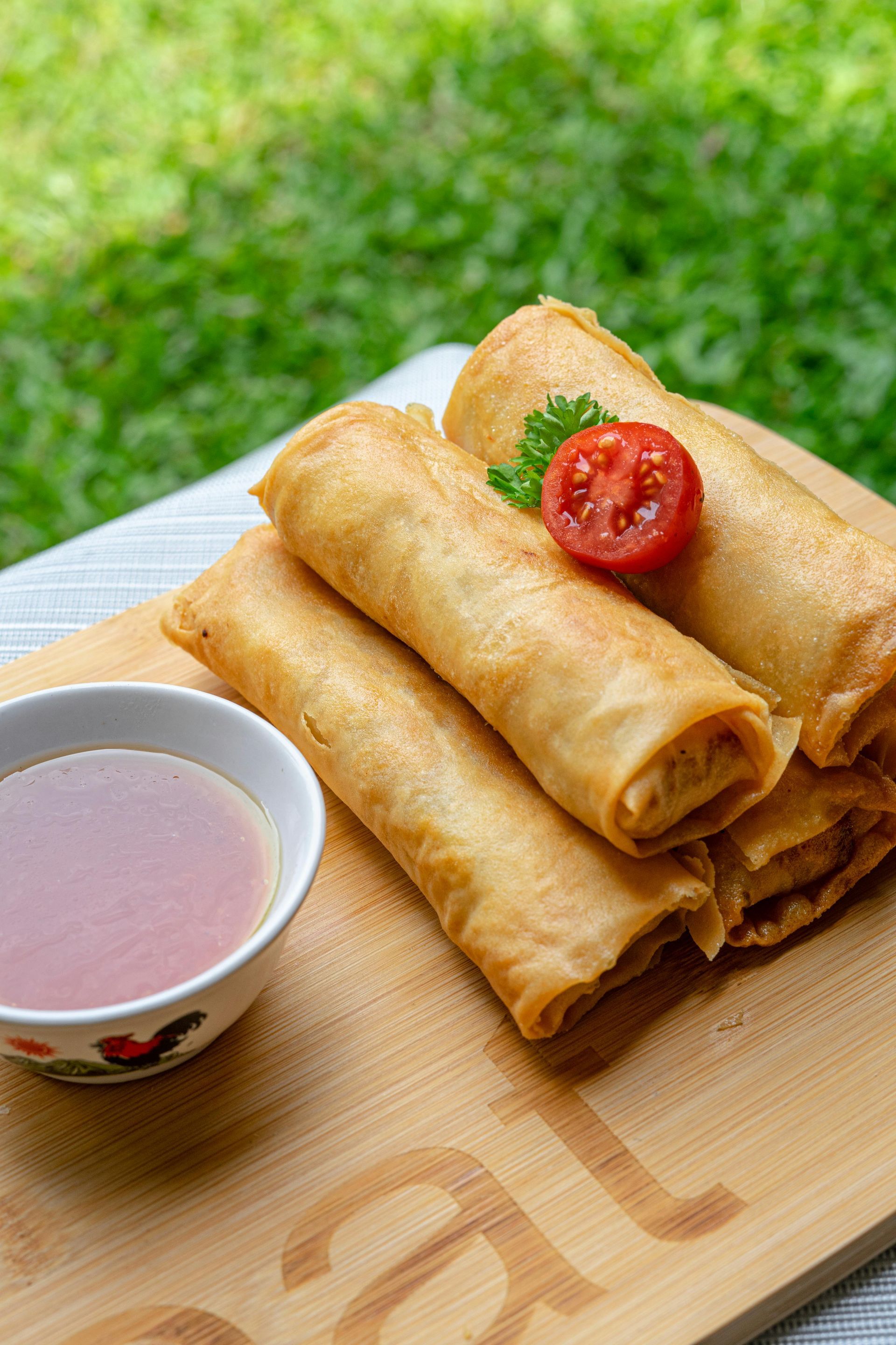 A wooden cutting board topped with spring rolls and a bowl of dipping sauce.