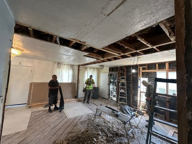 Room during renovation with exposed ceiling beams and three people inside.
