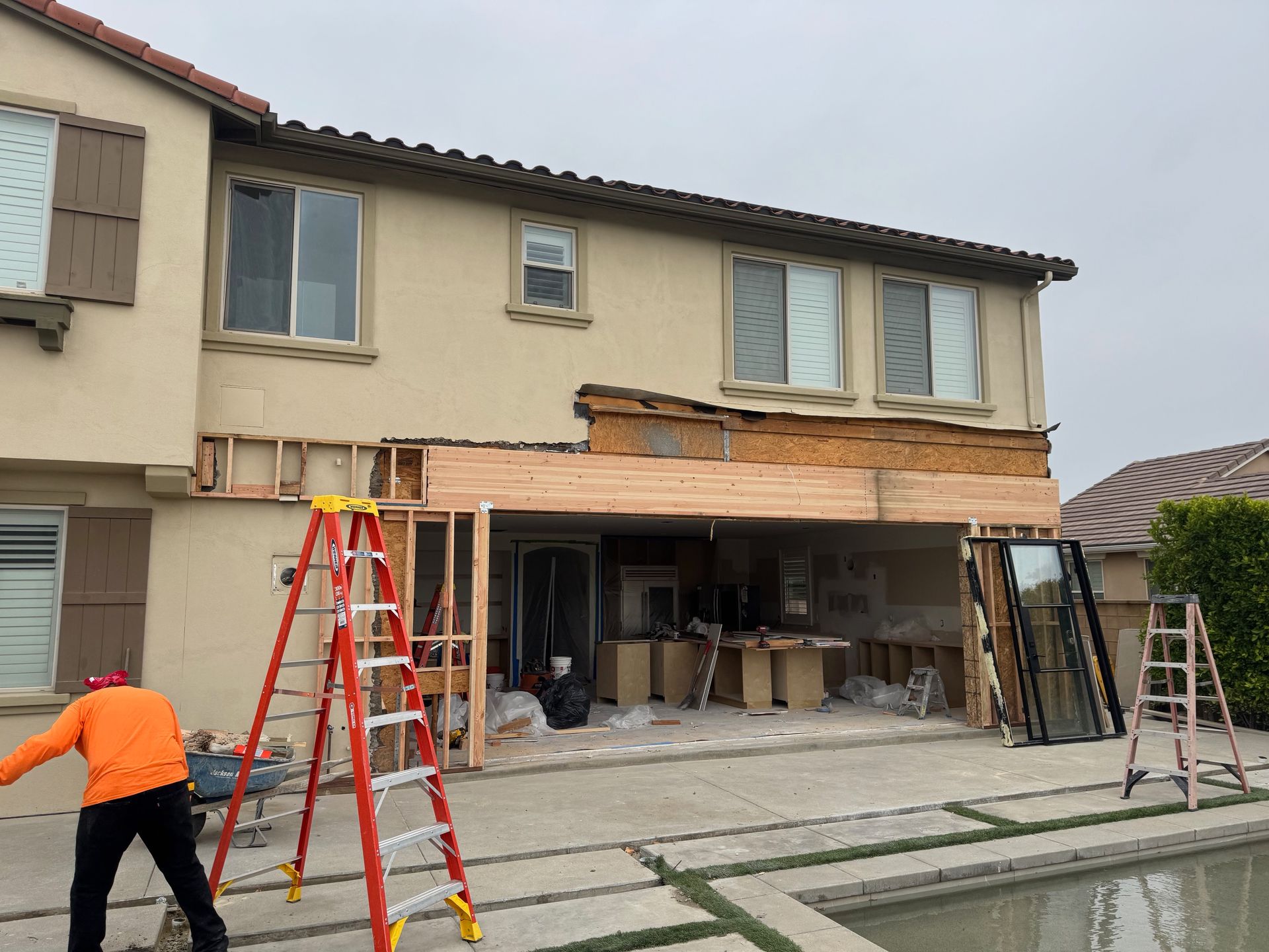 Construction on a two-story house with a partially built-out patio area; a worker stands near a ladder.