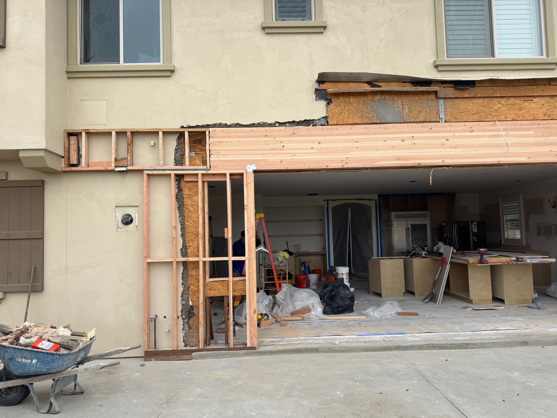 Exterior of a building under construction, showing exposed framing and garage interior. Construction debris in foreground.