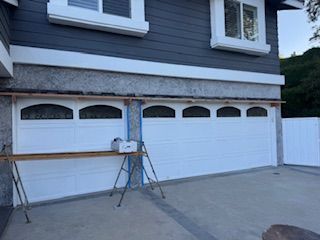 White garage doors on a gray house, construction underway with tools visible.