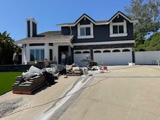 House exterior with construction debris in driveway; two-story, blue siding, white trim, gray garage door, sunny day.