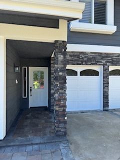 Gray house exterior with white trim, a front door, and garage doors.